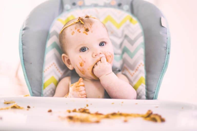 Bebé en la trona comiendo espaguetis con la mano manchada de tomate