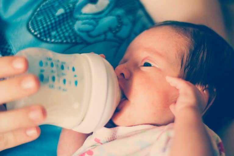 Un bebé recién nacido come la fórmula de un biberón por sí mismo sin la  ayuda de las manos. Un niño bebe la mezcla de leche de una botella tumbada  en la