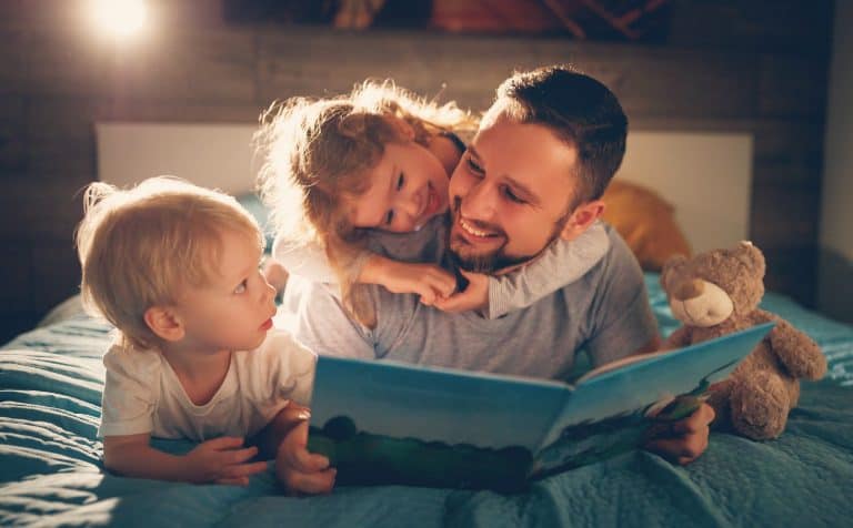Niños leyendo un libro con su padre en la cama