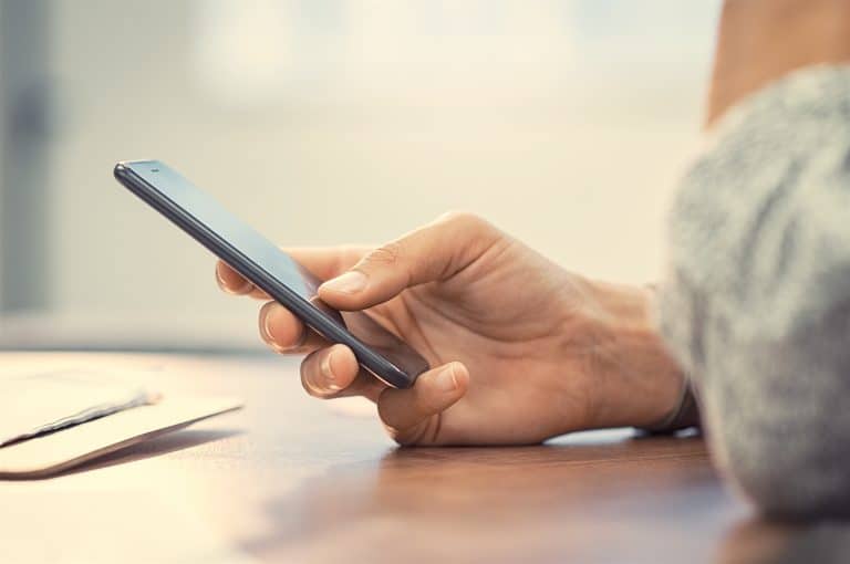 Closeup hand of woman using smartphone on wooden table. Businesswoman typing text message on smart p