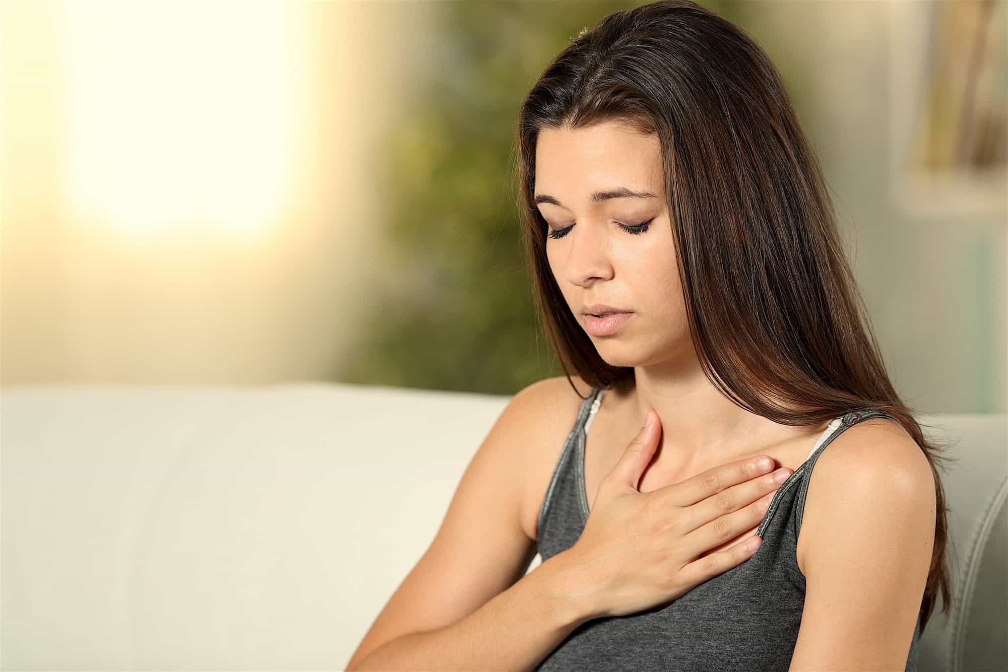 Girl Having Respiration Problems Touching Chest Sitting On A Couch In The Living Room At Home