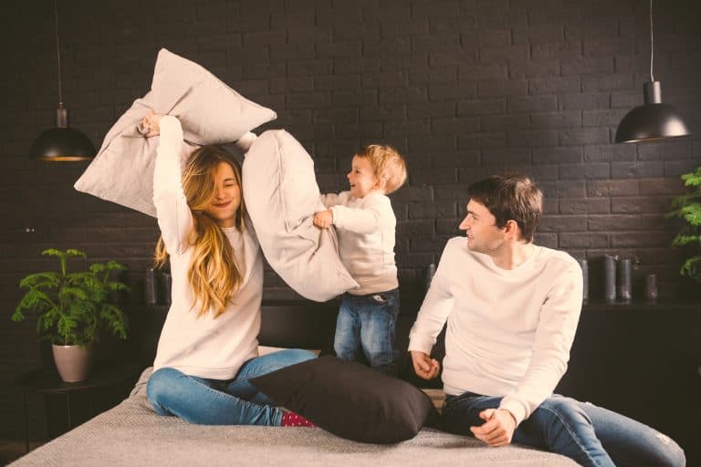 Family Having Funny Pillow Fight On Bed. Parents Spending Free Time With Their Son. Young Family Bei