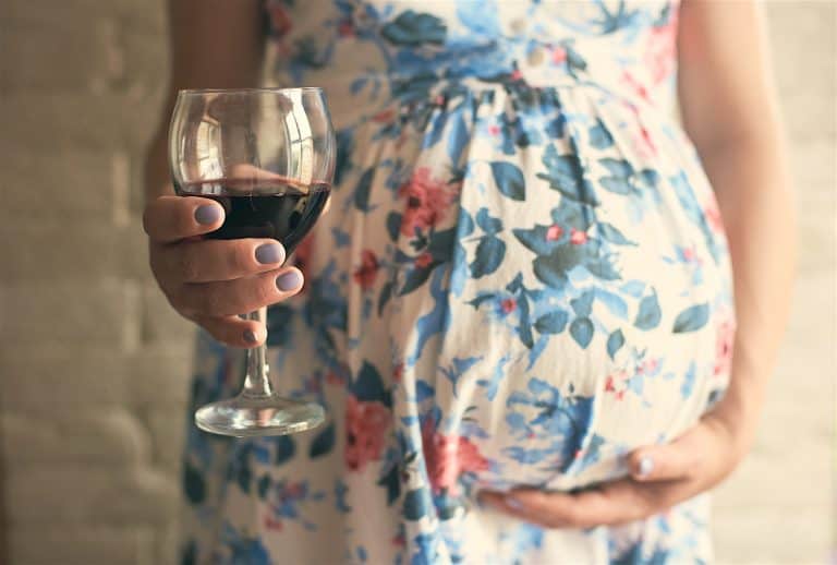 Selective Focus Of Glass Of Wine In Hands Of Pregnant Woman. Future Mother Embracing Belly And Drink