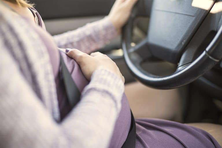 A pregnant woman driving a car buttoned up belt